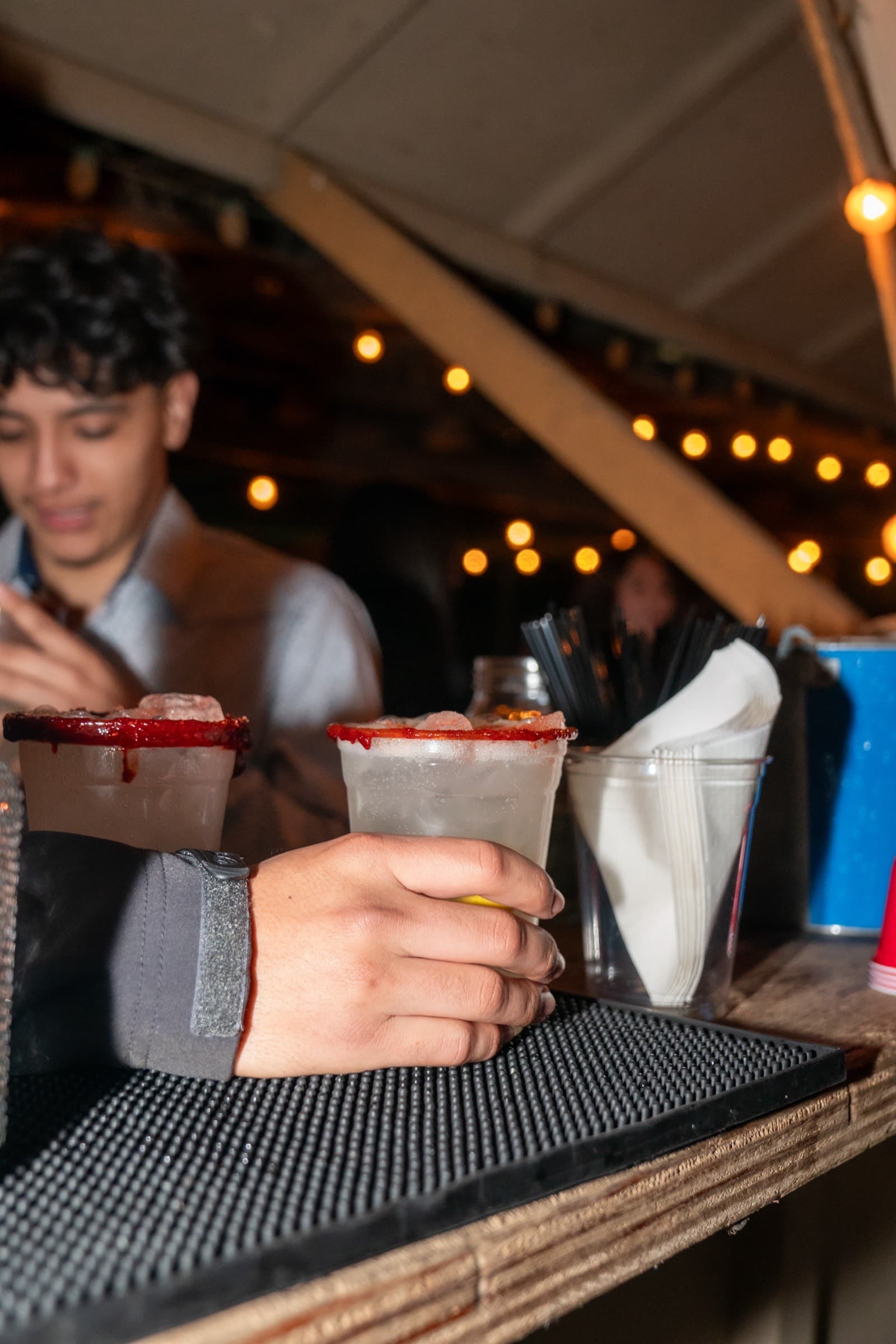 Rimdrip bartender at twilight under string lights serving micheladas